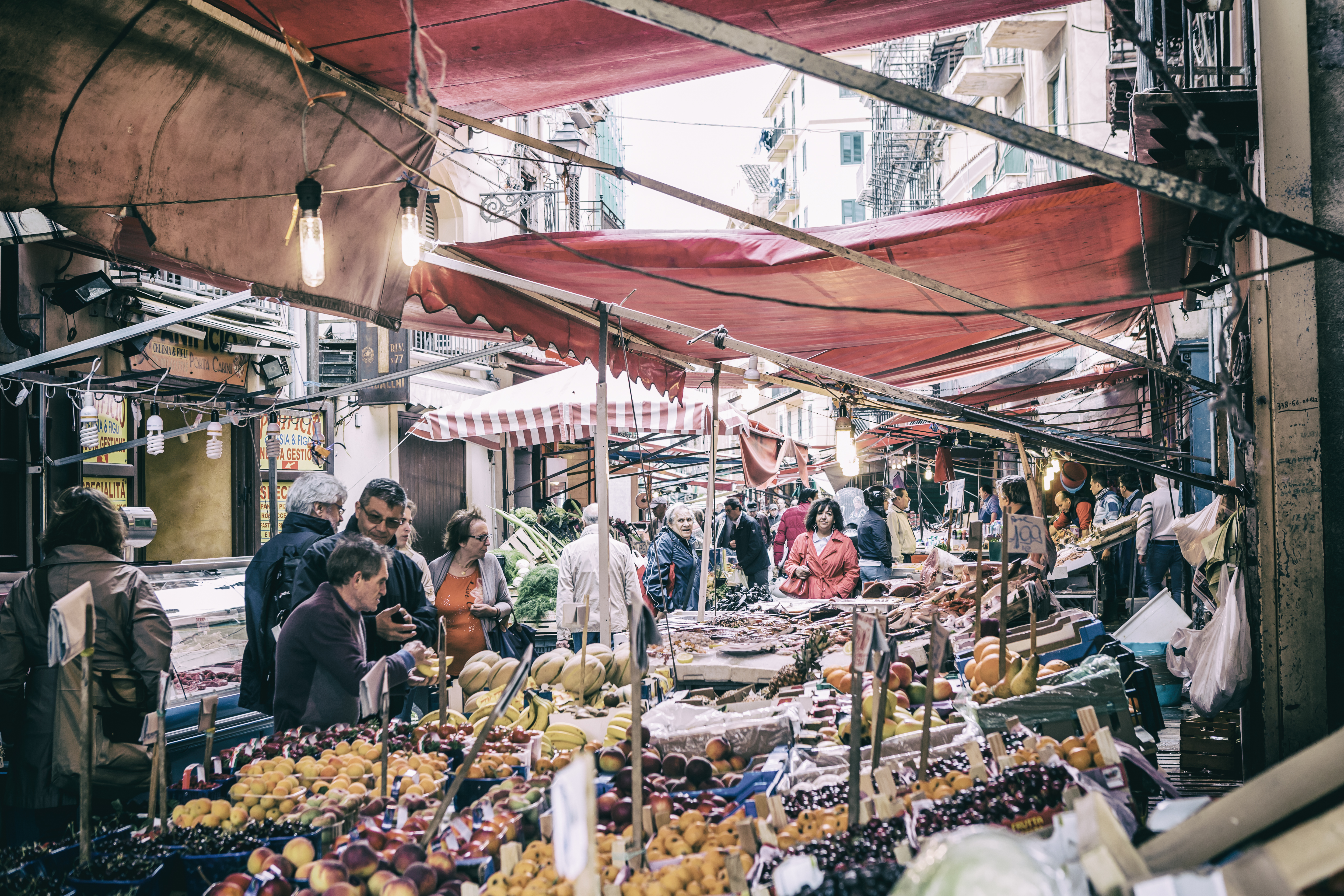 Fruit and vegetable market in Sicily, underneath red awnings in a narrow street