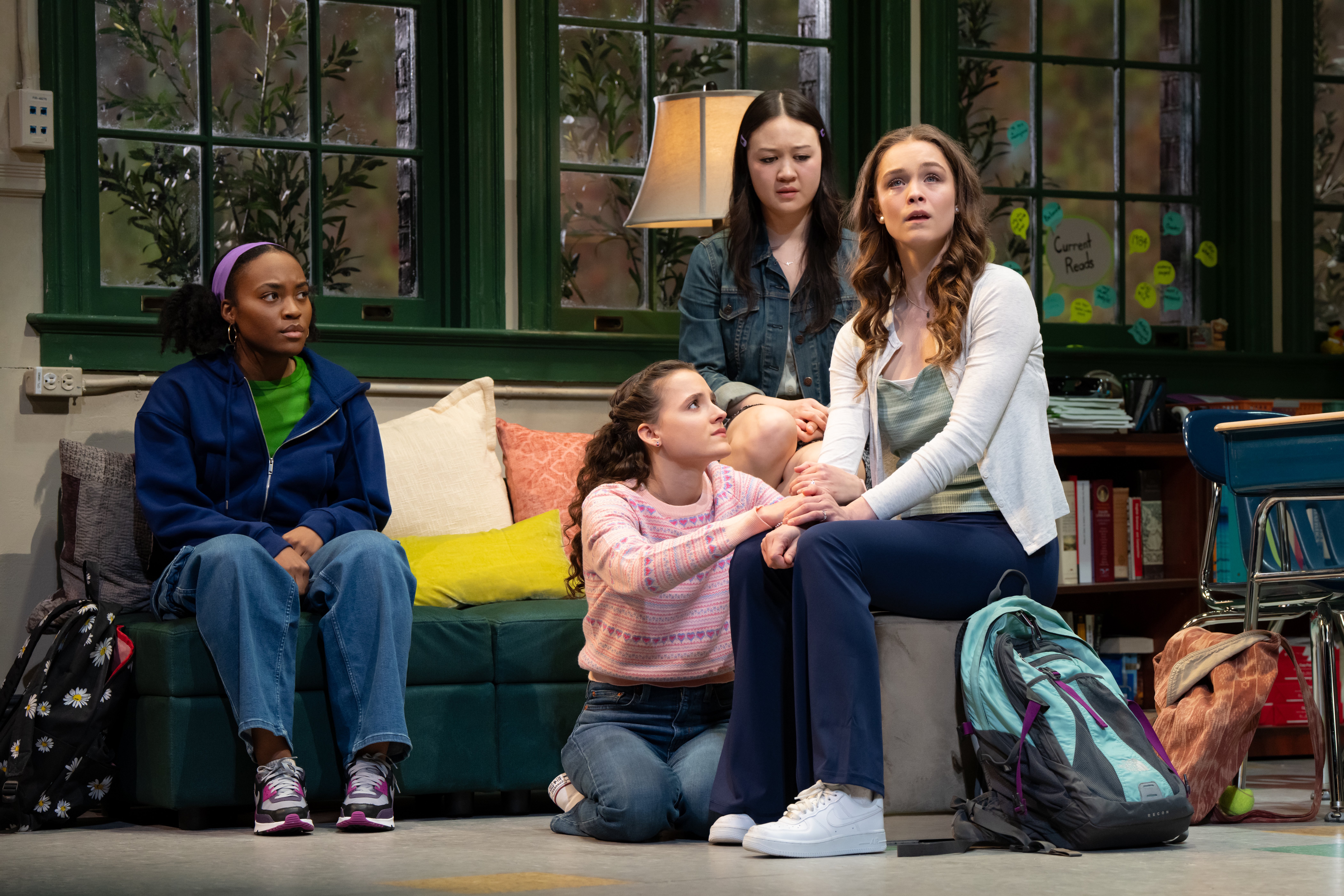 four teenage girls look concerned sitting on a couch in a classroom in the play john proctor is the villain