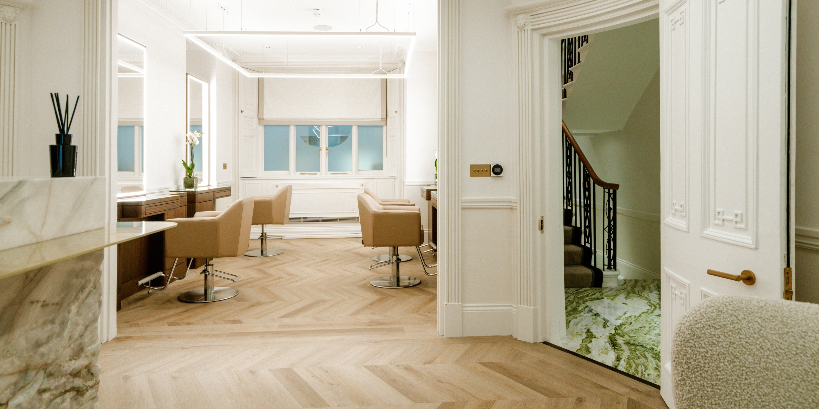 A softly lit, wood and marble-clad beauty salon with leather, cappuccino-shaded chairs, and wood and wrought iron staircases.