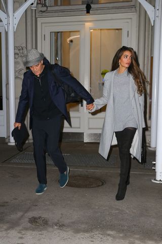 Amal Clooney and George Clooney walk out of a building in New York City holding hands, while Amal wears Taylor Swift's outfit formula of a sweater dress and thigh high boots