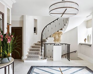 Traditional, large white entryway with curved staircase, classical sculpture on table,