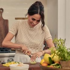 Meghan Markle chopping food on a table in With Love, Meghan