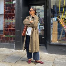 emily wears jeans, button down, trench coat, wine colored flats and a large brown tote