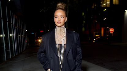Rihanna in lingerie, blue jeans, pearl necklaces, and a black maxi coat