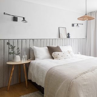 White bedroom with elongated grey headboard, modern wall lights and woven ceiling light