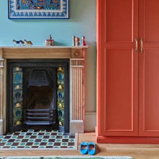 bedroom with a bright orange painted wardrobe beside a fireplace with classic tiled hearth and surround