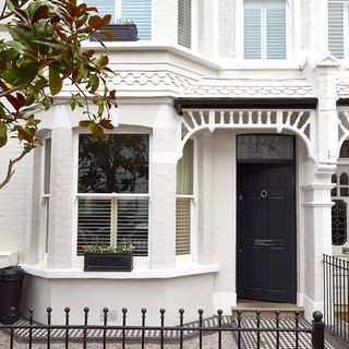 Victorian white house with black door and tree in garden