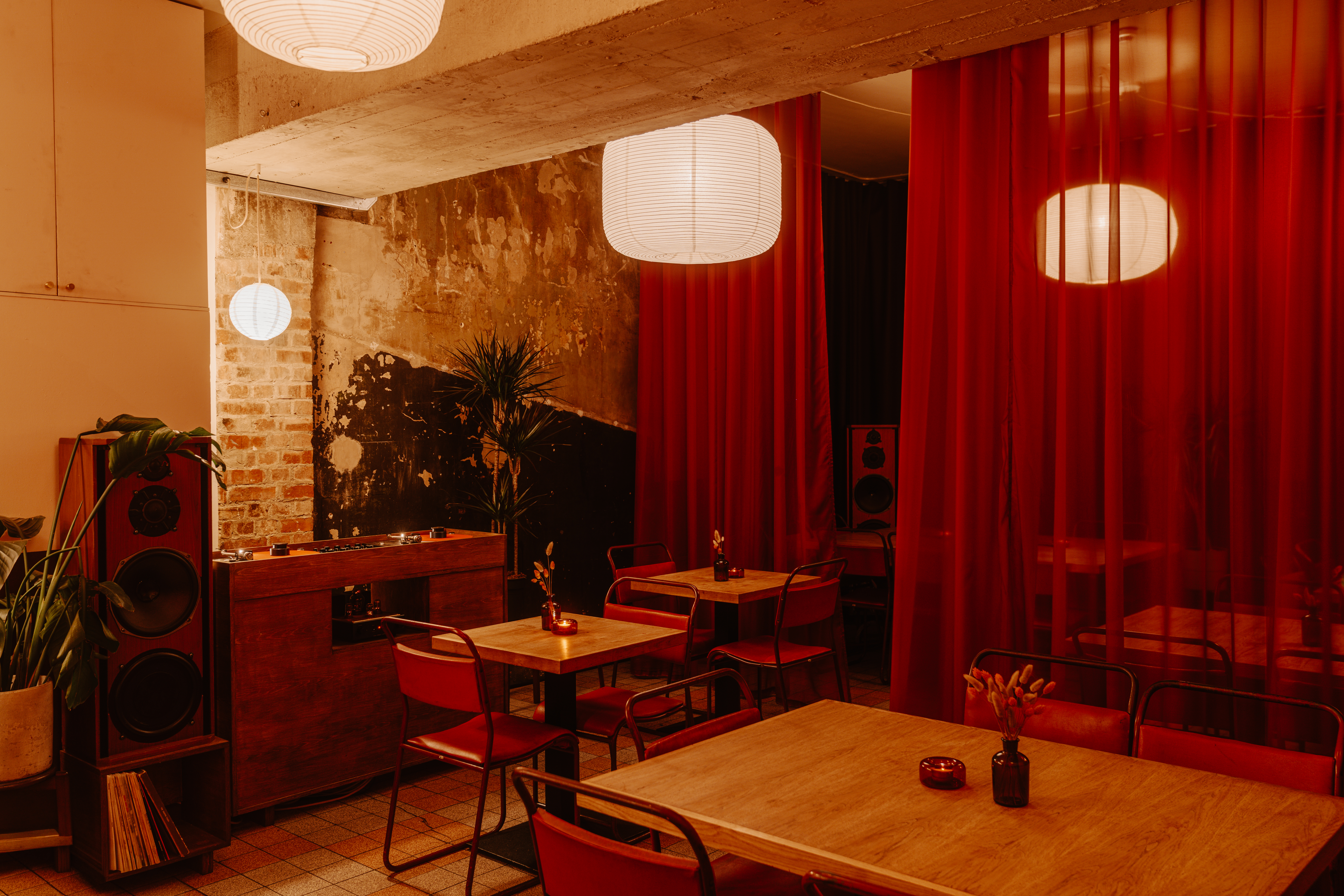 An interior shot depicting the warmly decorated spaces of a listening bar, with pendant paper lanterns, essential furniture, red curtains, and plenty of records hanging on the walls.
