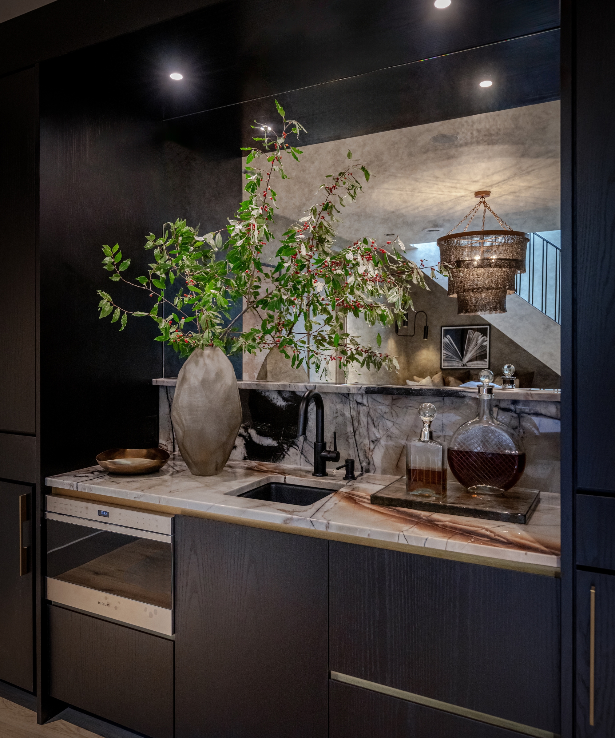 A dark home bar with a mixed material backsplash, half marble, half mirrored
