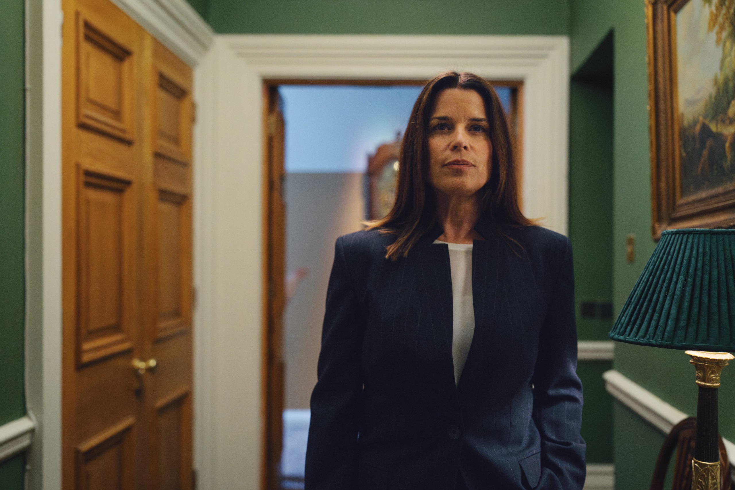 neve campbell wears a blazor as she walks down a regal looking hall in a first look at her new role in black doves season 2
