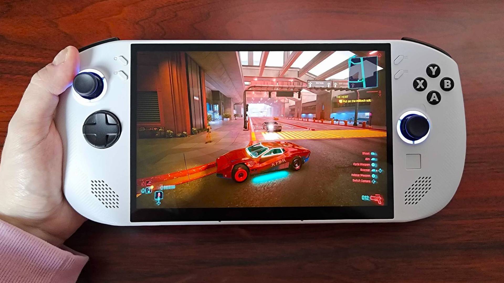 Hand holding Lenovo Legion Go S with Cyberpunk 2077 gameplay on screen featuring red sports car on road.