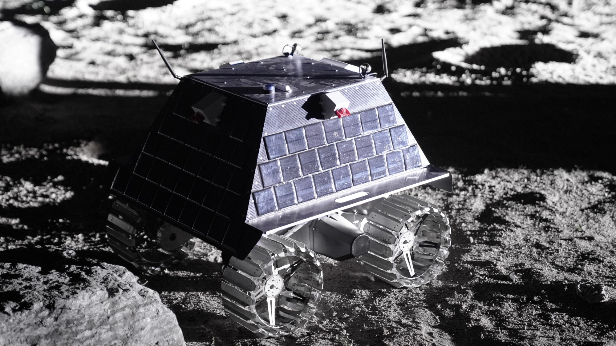 closeup photo of a small four-wheeled rover rolling across a simulated lunar landscape