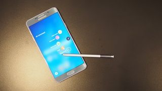 En Samsung Galaxy Note 5 ligger på ett guldigt bord med skärmen aktiv och vänd uppåt tillsammans med sin tillhörande stylus.