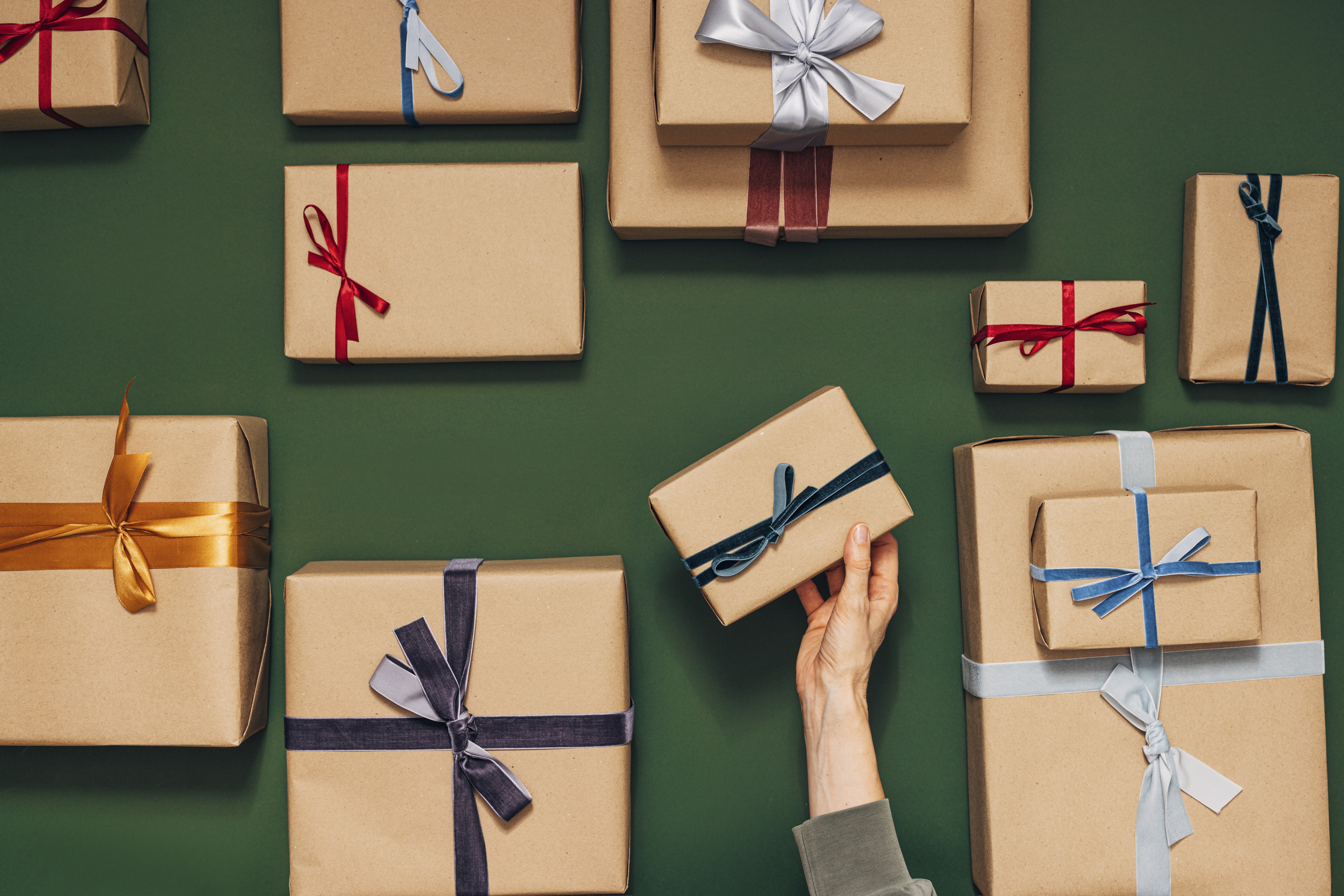 Presents — on a green table — in multiple sized wrapped in brown paper and jewel-tone ribbon