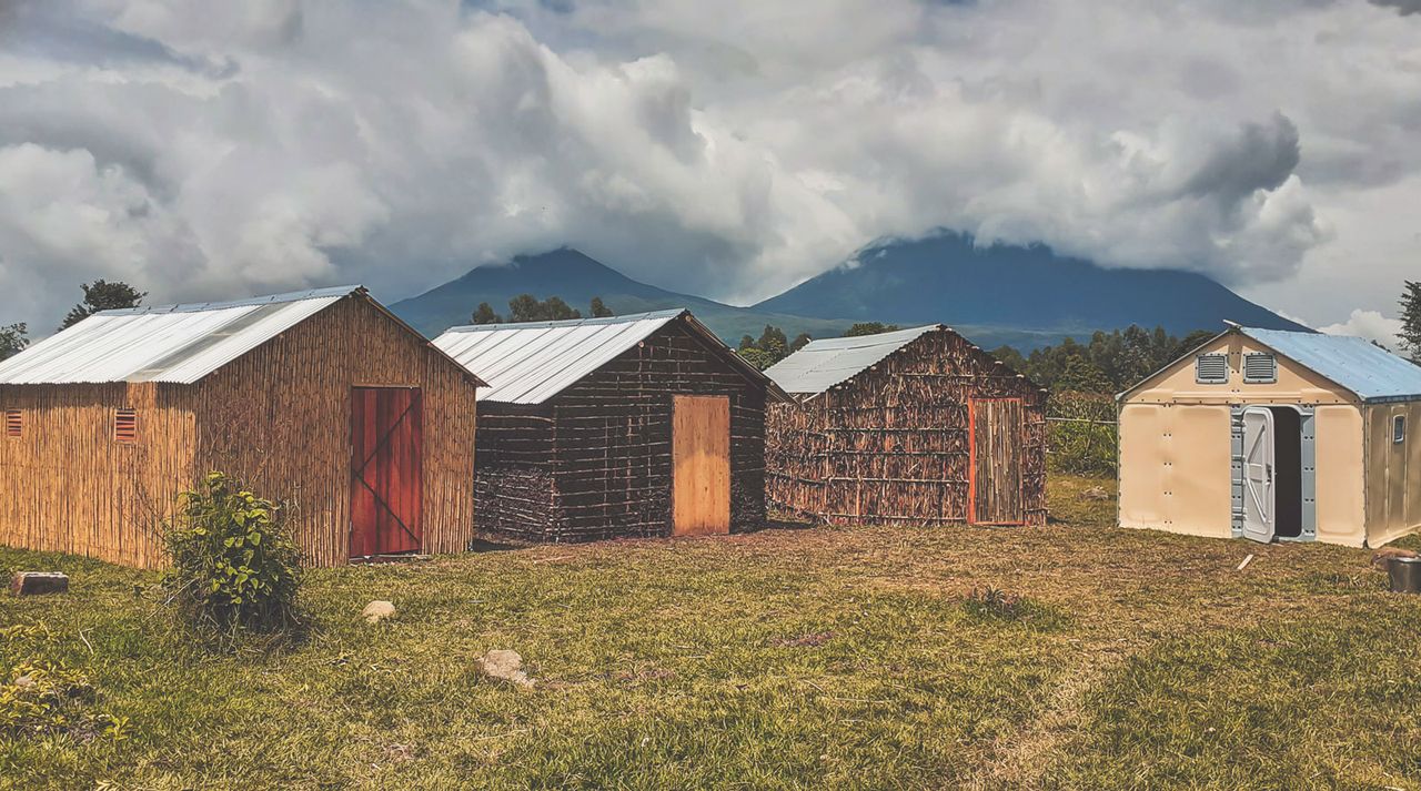 Four shelters built from wood in Rwanda in front of mountains