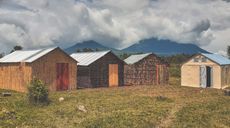 Four shelters built from wood in Rwanda in front of mountains