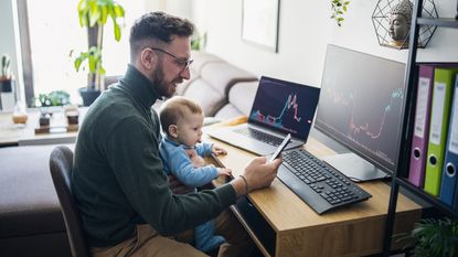 A man holds a baby as he works at his computer.