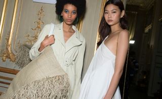 Models wear creme trenchcoat with fringed bag and white dress