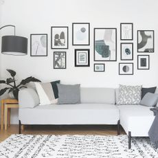 White painted living room with a grey sofa and a gallery wall behind it, and a white and black berber rug on the floor