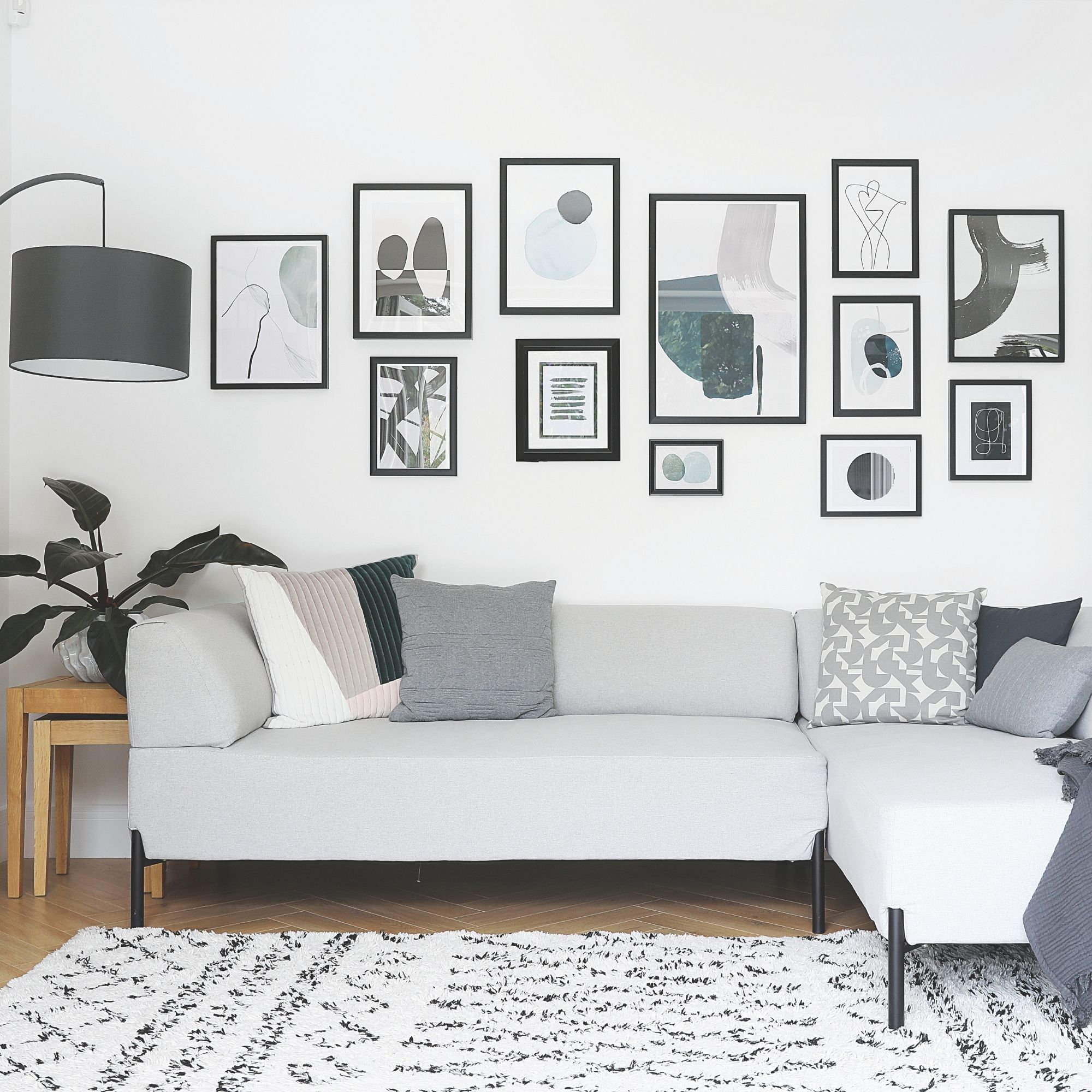 White painted living room with a grey sofa and a gallery wall behind it, and a white and black berber rug on the floor