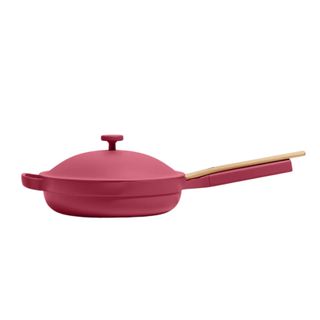A burgundy Our Place pan with a lid and wooden spoon