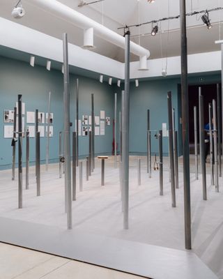 A site-specific installation features chrome poles standing on a square platform.