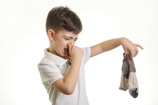 child holding nose as he holds a pair of dirty socks in his hand