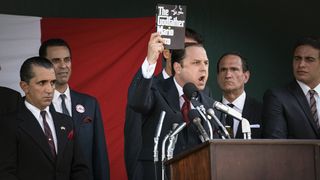Giovanni Ribisi as Joe Colombo holding up a book of The Godfather at a rally in The Offer