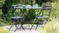 A black metal bistro set in a leafy green courtyard