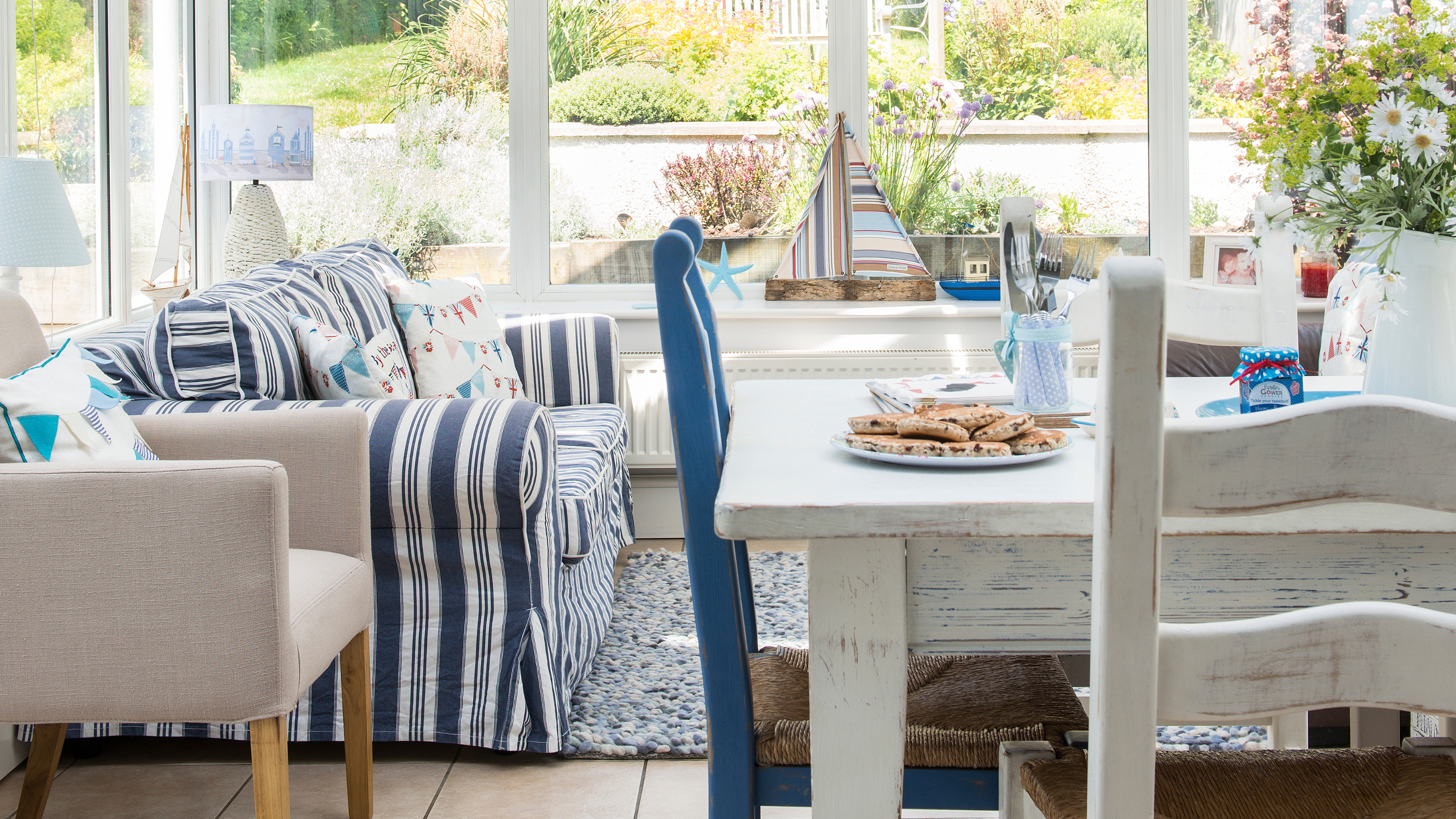 Glass panelled conservatory, rustic dining table and chairs, blue striped sofa, coastal accessories.