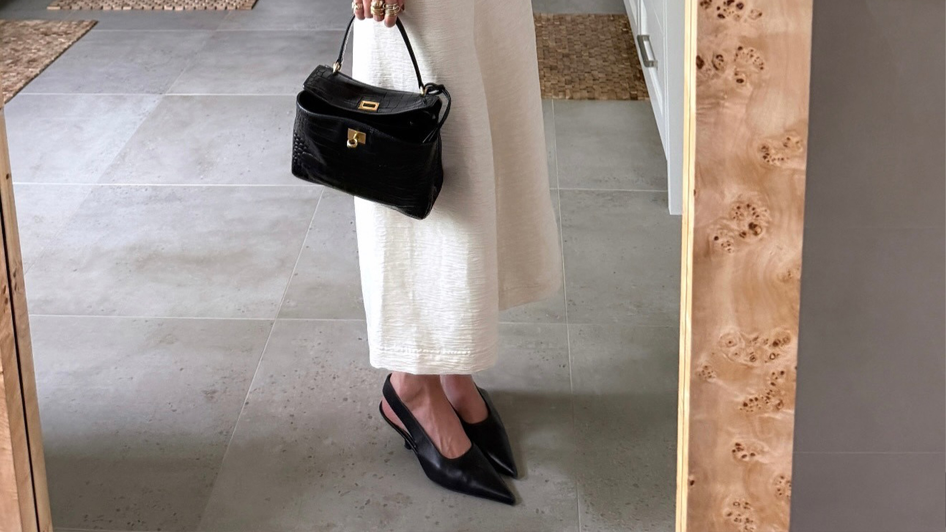 coco wears white dress, black sling backs, and black handbag
