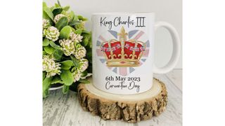 A King Charles coronation mug on a wood coaster.
