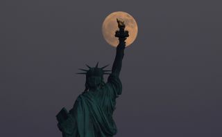 The Strawberry Moon rises behind the Statue of Liberty as the sun sets on the summer solstice in New York City on June 20, 2024, as seen from Jersey City, New Jersey.