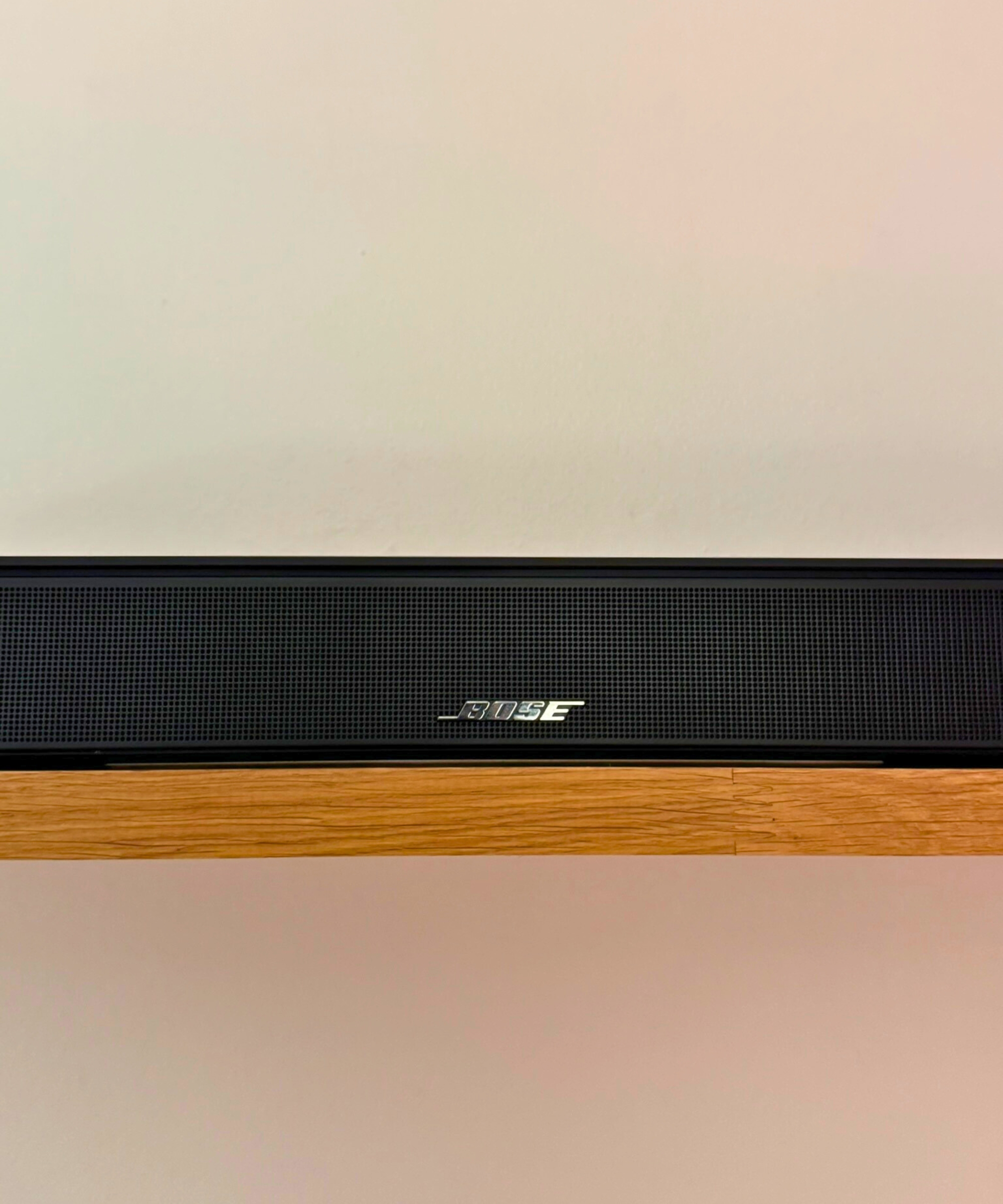 Closeup of the middle section of the Bose Smart Soundbar on wooden shelf in front of white wall.