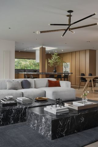 A modern open plan living room leading onto a kitchen with a floor to ceiling windows, a large white sectional sofa, and a dark marble coffee table