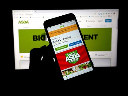 ASDA app seen on phone screen with ASDA website on computer screen in the background