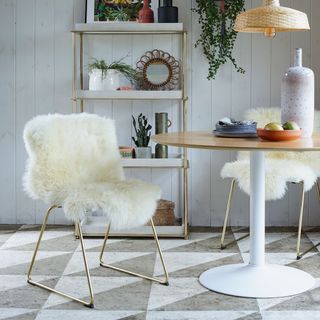 A small dining area with a round table, sheepskin covered chair and stenciled flooring