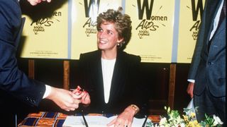 Diana sat at a desk while chatting to someone at a charity event for women suffering with AIDS