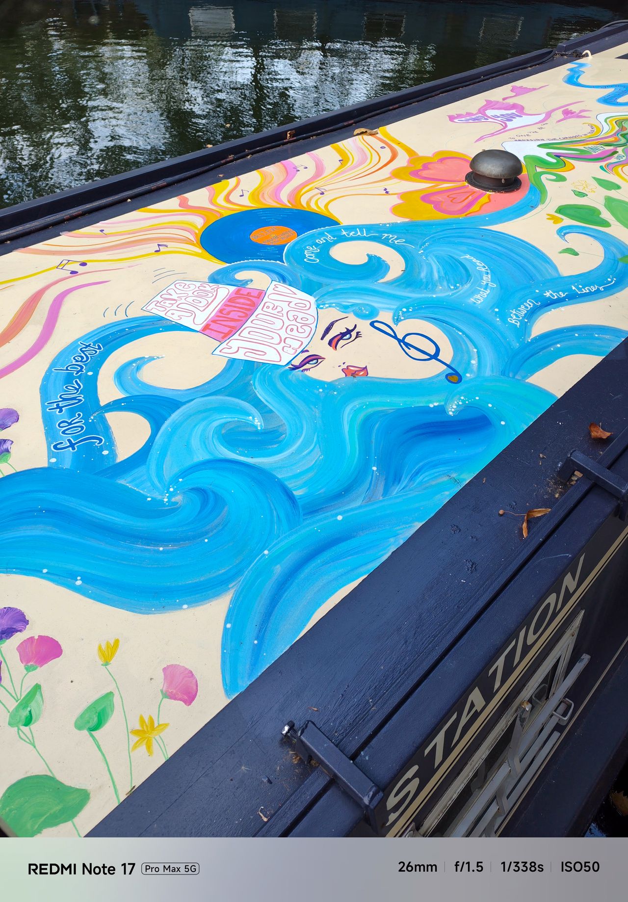 Colorfully painted narrowboat roof decorated with a blue-haired illustrated figure, flowers and musical motifs.