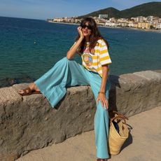 Influencer wearing bright blue pants with a striped T-shirt, sitting by the sea