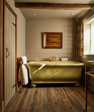 rustic bathroom with wooden beams, wooden floor, green walls and an avocado green freestanding bath tub