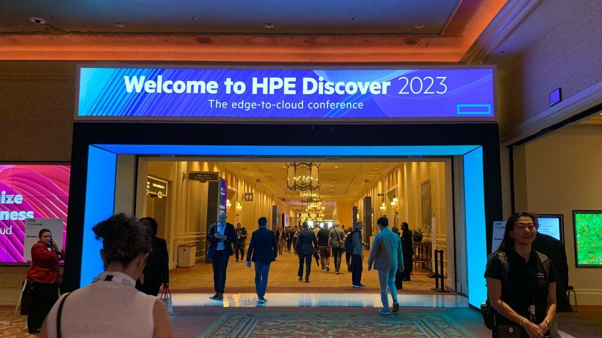 HPE Discover 2023: Shot of a blue illuminated sign in a hotel welcoming delegates to the HPE Discover 2023 event, with people walking down a long hallway travelling to scheduled sessions