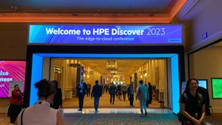 HPE Discover 2023: Shot of a blue illuminated sign in a hotel welcoming delegates to the HPE Discover 2023 event, with people walking down a long hallway travelling to scheduled sessions