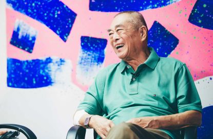 Portrait of Chinese abstract artist Hsiao Chin with one of his large, vivid paintings seen in the background