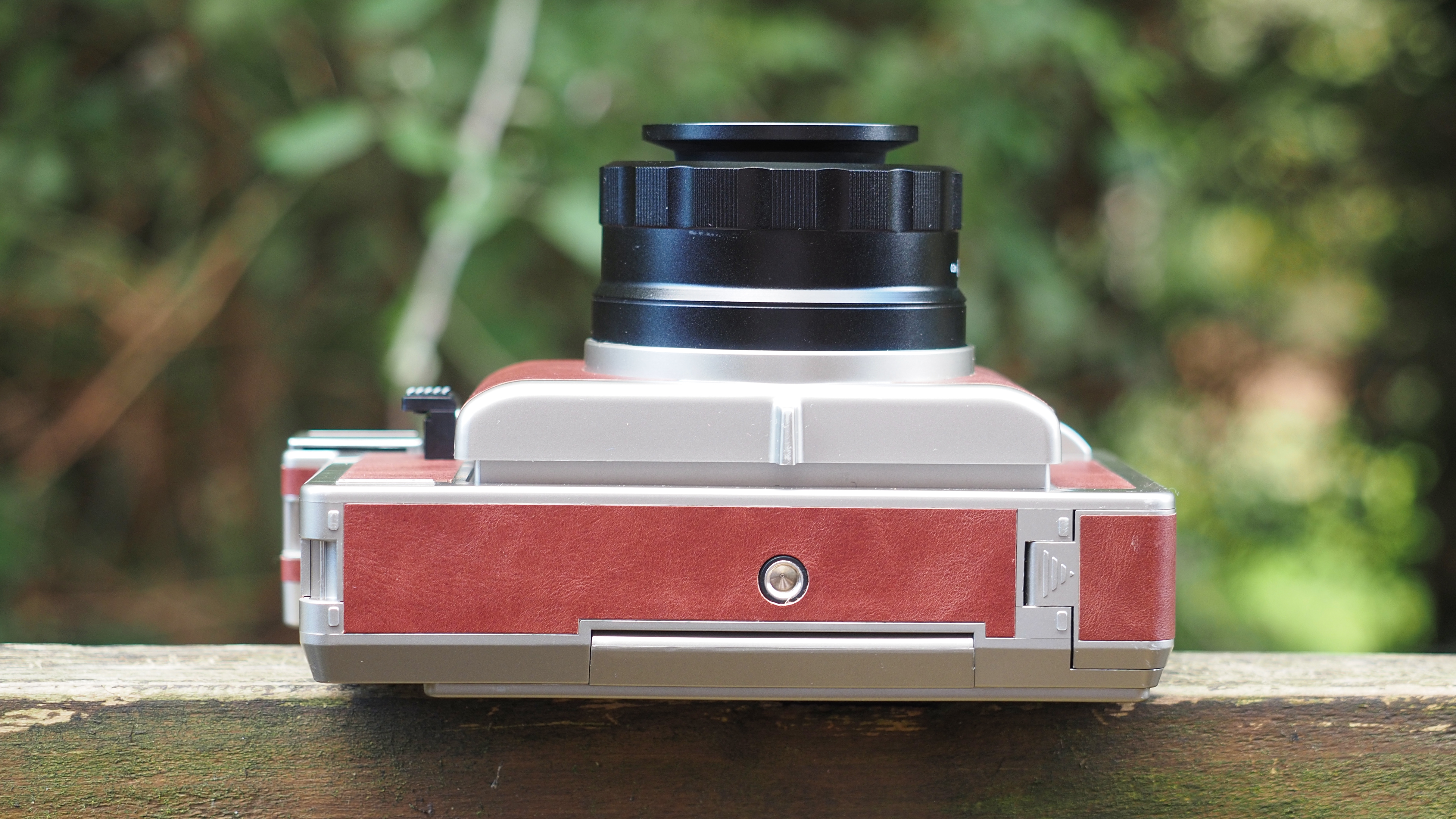 Lomo'Instant Wide Glass camera, sitting on a wooden surface, outdoors against a wooded background