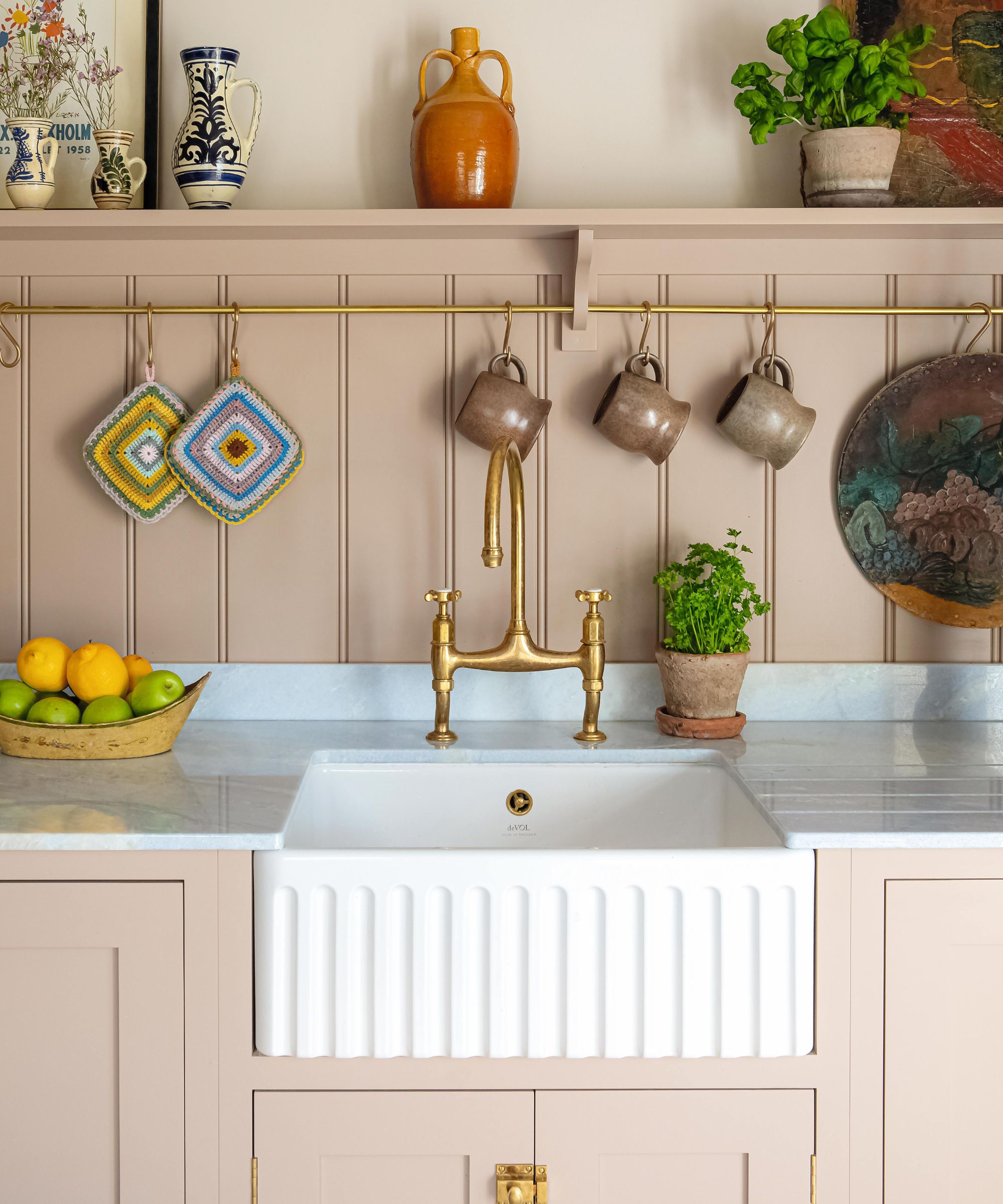 a pale pink painted in-frame kitchen with a tongue and groove paneled splashback, open shelving, and a fluted butler sink