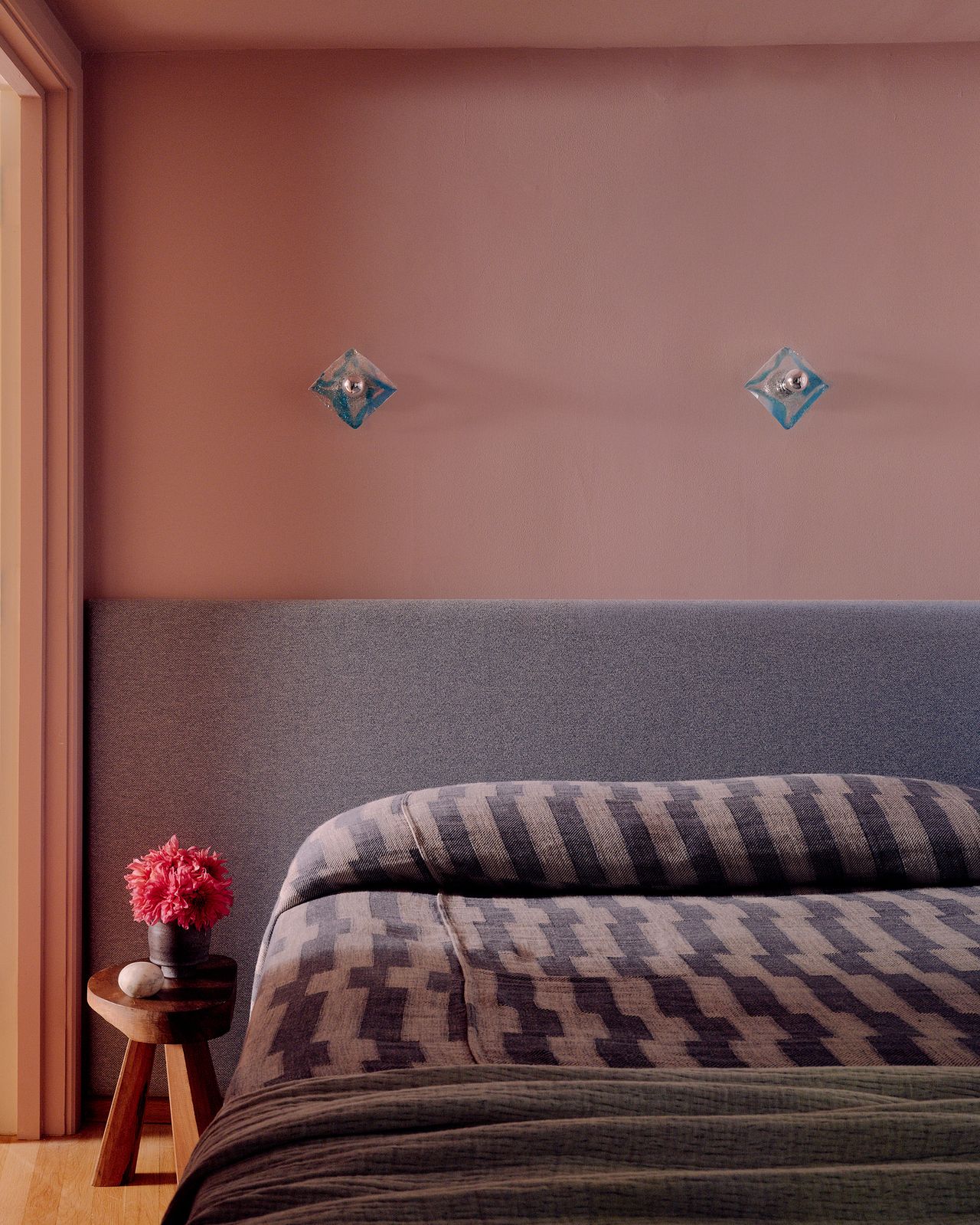 Image of a room painted in a pink terracotta color with a bed that has a gray extended headboard and purple and pink bedding.