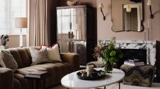 Image of a neutral living room with taupe walls and a white and black marble fireplace. There is a modern, curved sofa with a white porcelain coffee table in front.