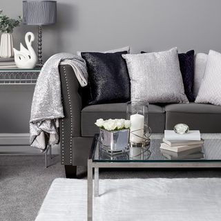 Grey and white living room with grey couch and cushions and a glass and silver coffee table