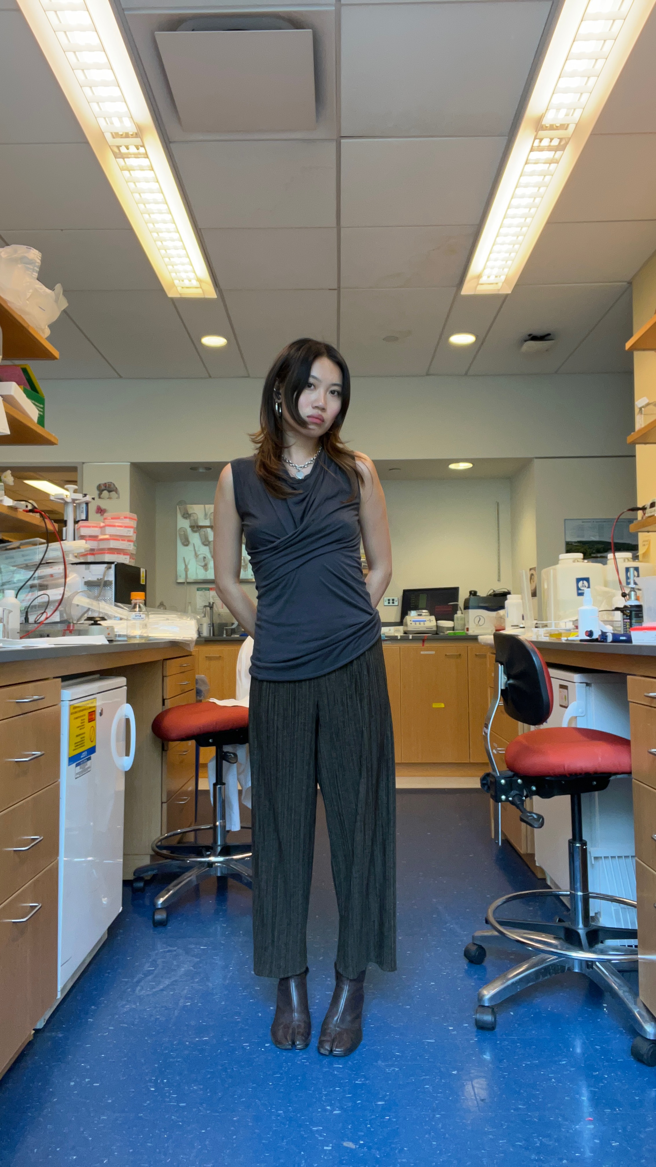 Vivan Li in a black top and pleated pants and black boots in a science lab